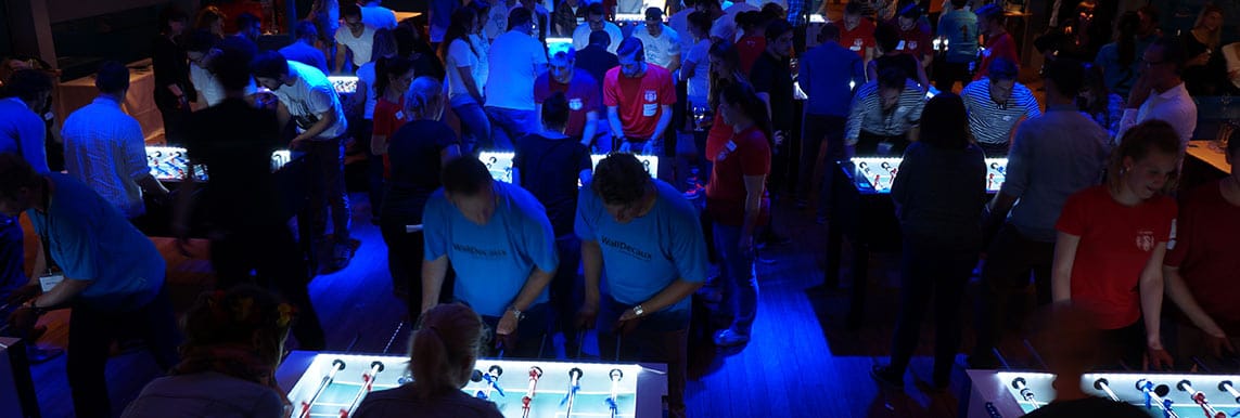 Menschen spielen an einem hell beleuchteten Tischkicker auf einem Event